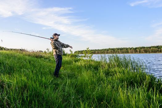 bearded man in a blue baseball cap on the river throws a spinning fishing