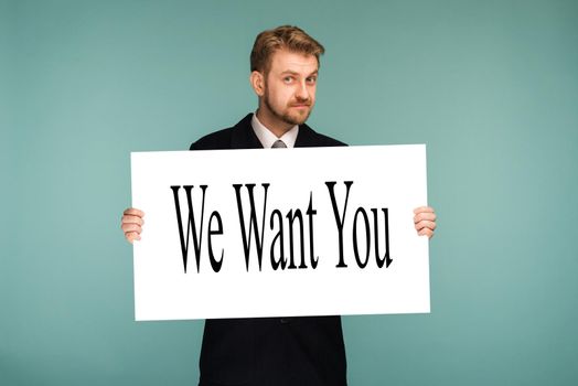 Happy smiling young business man showing signboard with sign We Want You, on blue background