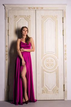 Beautiful girl in long classic red dress posing near old luxury doors. - image