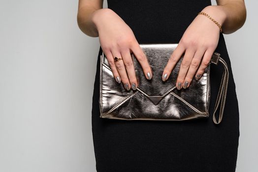 Fashion woman hold silver clutch in hand bag near gray background. Close up stylish accessory