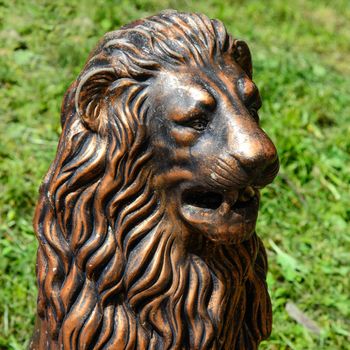 gilded sculpture of a lion&#39;s head set in a park on the green grass