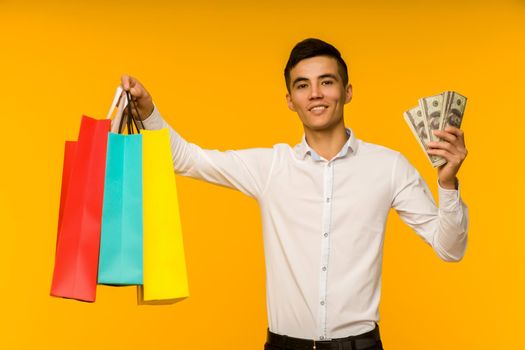 Young asian man showing his shopping bag and money on yellow background