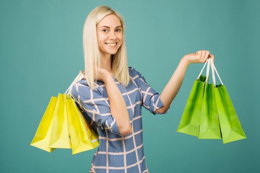 Happy girl in a checkered blouse holds shopping bags on blue background