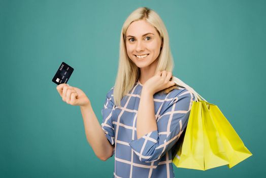 Happy girl in a checkered blouse holds credit card and shopping bags on blue background