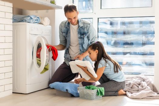 Happy family man father householder and child daughter in laundry with washing machine