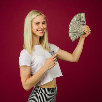 Young woman pointing towards a stack of money with her finger isolated on ruby background - Image
