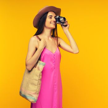 Happy girl in a pink dress and sunglasses holding camera on a yellow background- image toned
