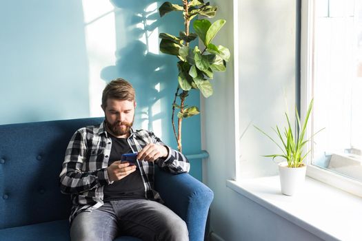 Man playing online games with a smart phone sitting on a couch at home