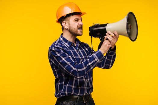 Angry worker man in orange helmet with a megaphone on yellow background - Image