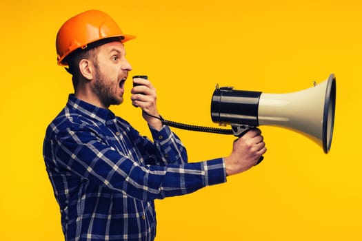 Angry worker man in orange helmet with a megaphone on yellow background - Image Toned