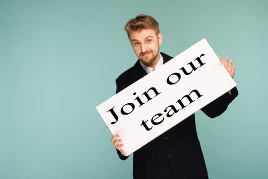 Happy smiling young business man showing signboard with sign Join Our Team, on blue background