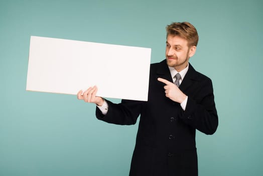 Happy smiling young business man points finger blank signboard, on blue background