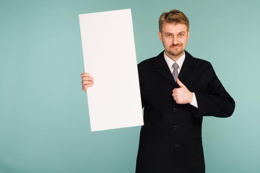 Happy smiling young business man showing blank signboard thumbs up, on blue background