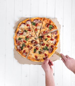 hands taking a piece of pizza top view on white wooden background