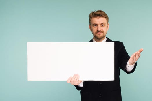 Happy smiling young business man showing blank signboard, on blue background
