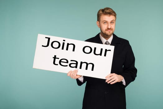 Happy smiling young business man showing signboard with sign Join Our Team, on blue background