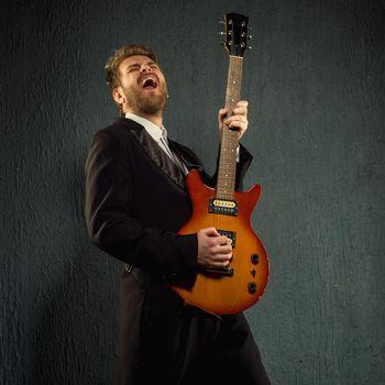 Guitar player with beard and black tailcoat emotionally plays music