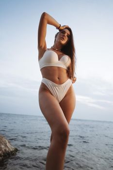 Sexy beautiful woman in white swimwear at the sea coast on sunset