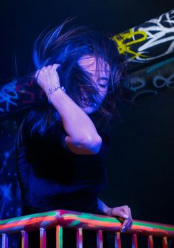 Belarus, Minsk - March 18, 2018: Young attractive brunette girl in neon light touches her hair thrown up with her hand while dancing in nightclub. Nightlife concept.