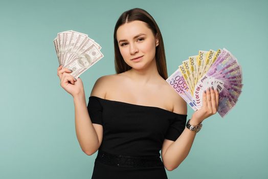 Close-up of young happy woman holding two fans of dollar and euro bills, looking at camera, isolated on blue background - Image