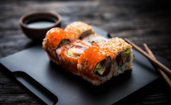 close up of sushi rolls on black tray and dark wooden table