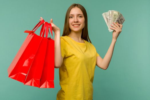 Photo of cheerful young woman holding fan of money and red shopping bags,isolated on blue background - image