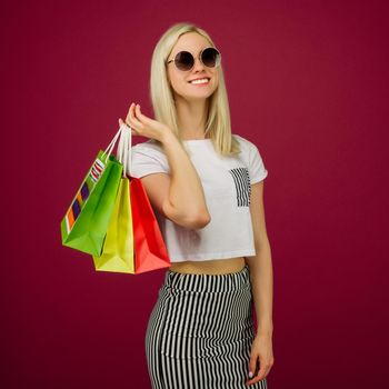 Happy girl in sunglasses holds shopping bags on ruby background