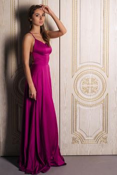 Fashion portrait of a woman in a beautiful long evening dress, near the big white doors. Luxurious interior, perfect figure and hair girl