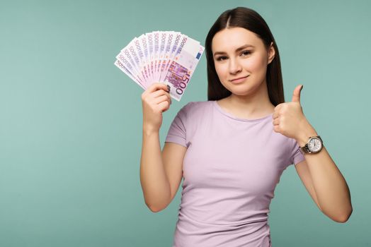 A young woman with dollars in her hands and showin g ok, isolated on blue background - Image