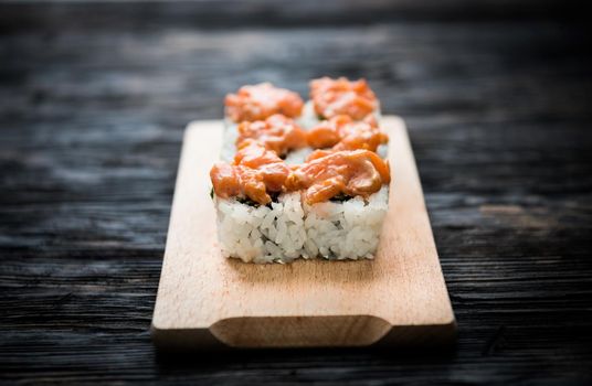 closeup of a set of sushi rolls with salmon topping on wooden board