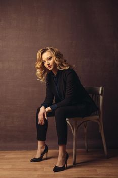 Young confident businesswoman sitting on the chair on gray background.