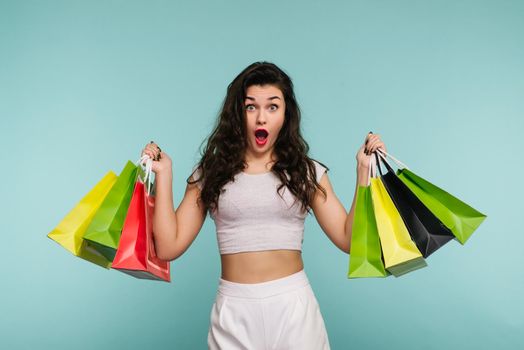 Young beautiful fashionable woman holding shopping bags over turquoise background - Image