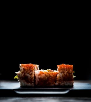 close up of sushi rolls on black tray and dark wooden background
