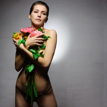 young sexy sensual woman or girl with brunette hair and pretty face topless holding flowers on naked body with panties on grey background.