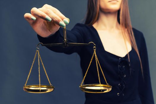 Serious woman holding the justice scale on dark background - image toned