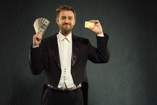 Positive man in a tailcoat offers a credit card and money. - image