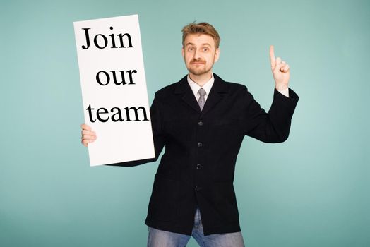 Happy smiling young business man showing signboard with sign Join Our Team, on blue background