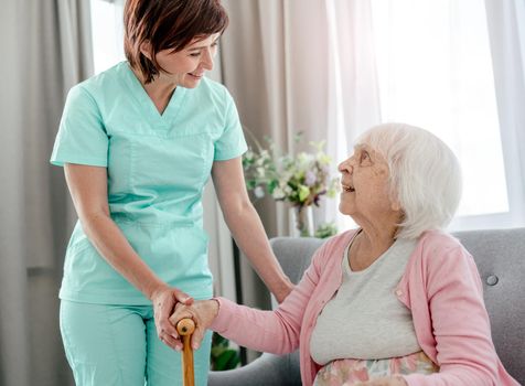 Elderly woman and nurse at home. Senior female person and healthcare worker girl talking