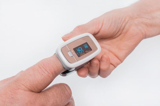 The hand of an elderly man inserted a finger into the pulse oximeter in the hand of an elderly woman on a white background.