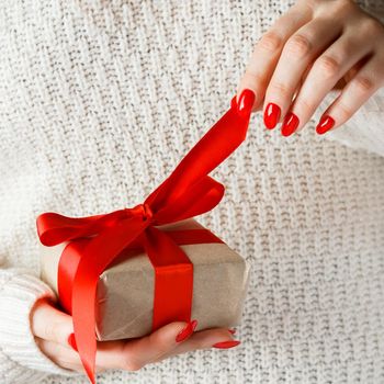 Gift with a red ribbon in hands on a white background. A woman unpacks a box with a surprise. Giving a gift for the holiday.