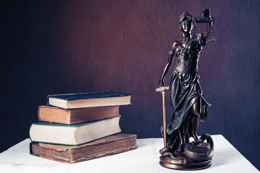 Themis figurine stands on a white wooden table next to a stack of old books. Scales Law Lawyer Business Concept. - Image