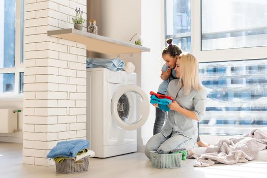 Young housewife and little girl doing laundry together