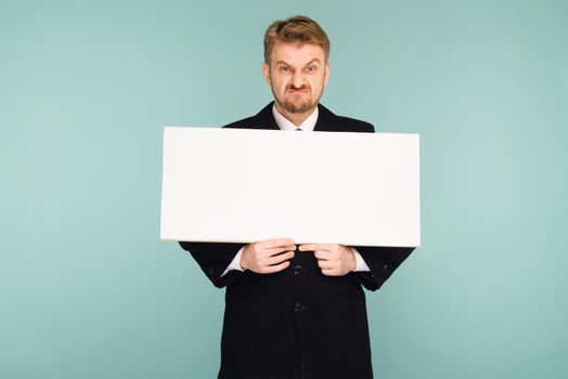 Angry beard young business man showing blank signboard, on blue background