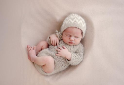 Newborn baby boy sleeping wearing knitted beige costume. Infant child kid napping during studio photoshoot