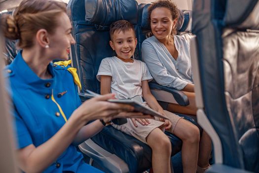 Female air hostess trying to entertain a kid on the plane by offering a book to read. Cabin crew provide service to family in airplane. Airline transportation and tourism concept
