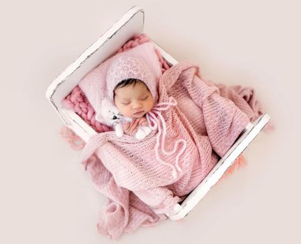Adorable newborn baby girl sleeping in tiny bed and holding knitted toy. Cute infant kid child napping