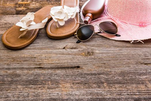 Beach accessories. Summer shoes and hat with sunglasses and suntan lotion on a wooden background
