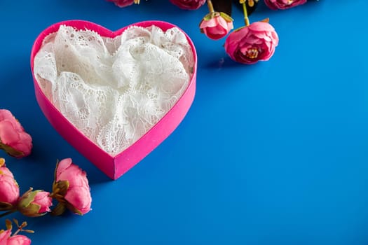 Pink gift box and flowers on a blue background. Beautiful pink heart-shaped gift box and flowers on a blue background. Place for text, design for valentines day.