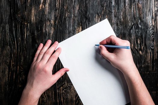 hands holding paper sheet and pen on dark wooden table top view