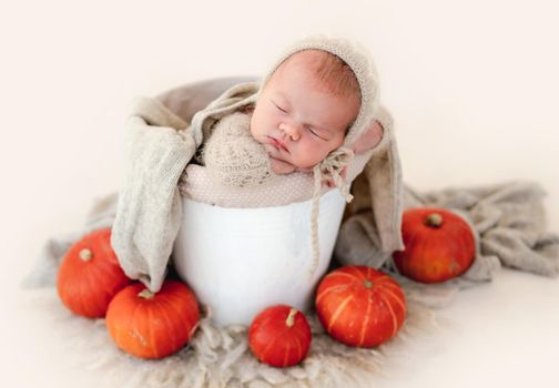 Newborn baby boy sleeping in basin decorated with pumpkins. Infant child kid resting during studio photoshoot